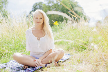 Young blonde woman sitting on blanket looking at camera smiling - CUF29188