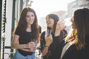 Drei junge Freundinnen lachen und unterhalten sich auf einem Balkon am Wasser - CUF29197