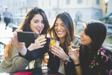 Drei junge Frauen kichern für ein Smartphone-Selfie im Hafencafé - CUF29199