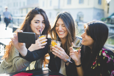 Three young women giggling for smartphone selfie at waterfront cafe - CUF29199