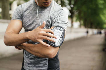 Cropped shot of male runner choosing music on smartphone - CUF29212