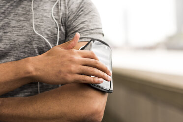 Ausgeschnittene Aufnahme eines männlichen Läufers, der die Musik auf seinem Smartphone-Armband auswählt - CUF29219