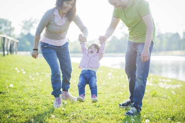 Mid adult couple swinging toddler daughter in park - CUF29260