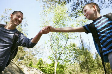 Male hiker giving son a helping hand in forest - CUF29274