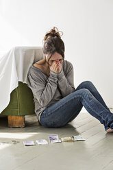 Mature woman sitting on floor in house, counting money, distressed expression - CUF29307