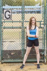 Young woman standing beside sports ground, London, UK - CUF29348