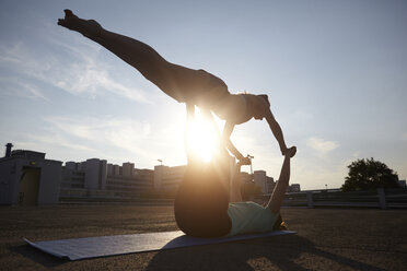 Zwei silhouettierte junge Frauen üben Yoga auf einem städtischen Parkplatz - CUF29379