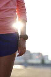 Ausgeschnittene Aufnahme einer jungen Läuferin mit Smartwatch im Sonnenlicht - CUF29381