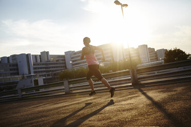Sonnenbeschienene Silhouette einer jungen Läuferin, die auf einem Hausdach läuft - CUF29382