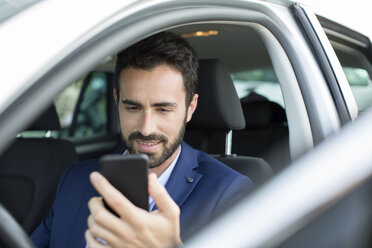 Junger Geschäftsmann liest Smartphone-Texte im Auto - CUF29448