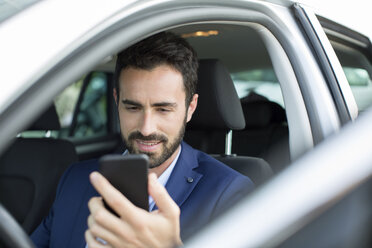 Young businessman reading smartphone texts in car - CUF29448