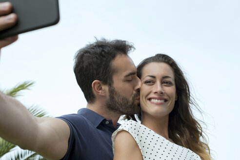 Junger Mann küsst Freundin auf die Wange für Smartphone-Selfie - CUF29463