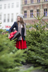 Mature woman with Christmas gift among Christmas trees - CUF29470