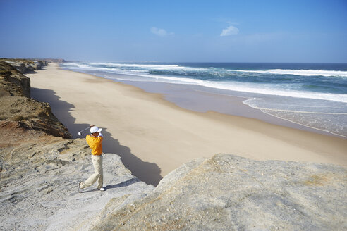 Golfer steht auf einer Klippe mit Blick auf den Strand und macht einen Golfschlag - CUF29491