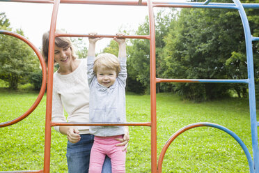 Mother and female toddler playing on park climbing frame - CUF29504