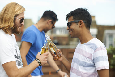Zwei männliche Freunde stoßen mit Flaschenbier auf einer Dachterrassenparty an - CUF29542