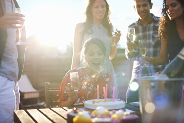 Friends at outdoor party blowing out candles on cake - CUF29564