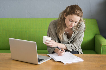 Young female designer making notes from office sofa - CUF29572