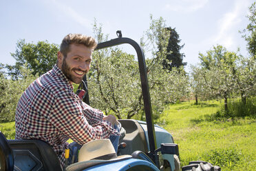 Young man sitting in tractor looking over shoulder at camera smiling - CUF29658