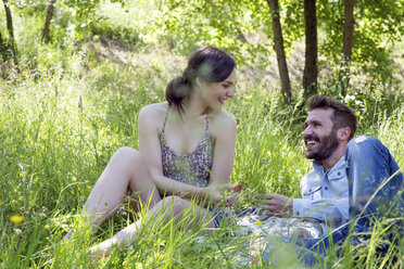 Junges Paar im Gras liegend, von Angesicht zu Angesicht, lächelnd Erdbeeren essend - CUF29661