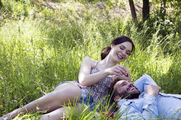 Junges Paar liegt im Gras und isst lächelnd Erdbeeren - CUF29662