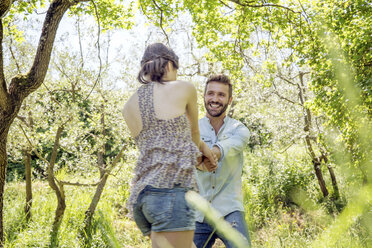 Young couple holding hands in forest fooling around smiling - CUF29665