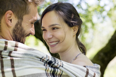 Kopf und Schultern eines jungen Paares, eingewickelt in eine Decke, von Angesicht zu Angesicht lächelnd - CUF29675