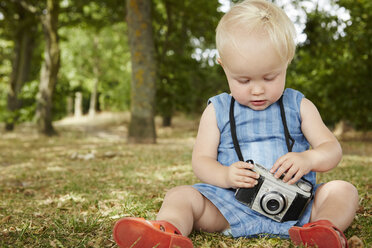 Baby-Mädchen sitzt im Gras und hält eine Filmkamera, die nach unten schaut - CUF29693