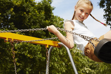 Girl with pigtails on swing looking at camera smiling - CUF29697