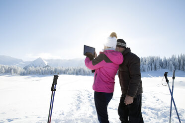 Rear view of senior couple on snowy landscape using digital tablet to take photograph of mountain range, Sattelbergalm, Tyrol, Austria - CUF29702