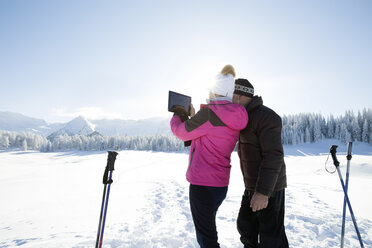 Rückansicht eines älteren Paares in einer verschneiten Landschaft, das ein digitales Tablet benutzt, um eine Bergkette zu fotografieren, Sattelbergalm, Tirol, Österreich - CUF29702
