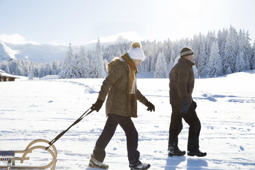 Side view of senior couple on snowy landscape pulling sledge, Sattelbergalm, Tyrol, Austria - CUF29703