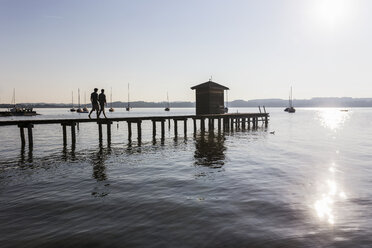 Silhouette eines Paares, das auf einem Steg am See zum Bootshaus geht, Schondorf, Ammersee, Bayern, Deutschland - CUF29731