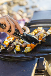 Young mans hand using tongs to turn sausages and kebabs on barbecue griddle - CUF29734