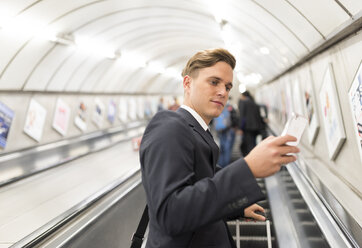 Geschäftsmann, der auf einer Rolltreppe eine SMS schreibt, London Underground, UK - CUF29758