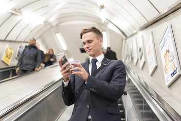 Geschäftsmann, der auf einer Rolltreppe eine SMS schreibt, London Underground, UK - CUF29759