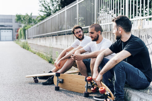 Seitenansicht von jungen Männern, die mit Skateboards auf dem Bordstein sitzen - CUF29788