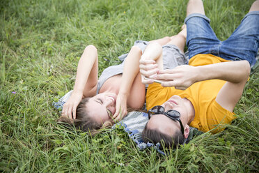 Junges Paar liegt im Gras auf einem Feld und schaut auf ein Smartphone - CUF29789