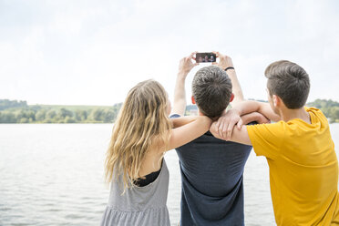 Drei junge Erwachsene nehmen ein Selbstporträt mit einem Smartphone auf, Rückansicht - CUF29794