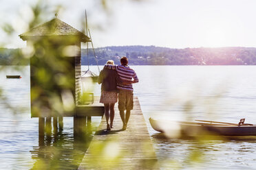 Rear view of young couple walking along pier on lake to boathouse, Schondorf, Ammersee, Bavaria, Germany - CUF29803