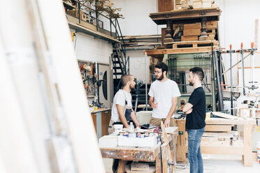 Friends standing around workbench in carpentry workshop talking - CUF29817