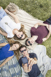 Group of young adults lying on picnic blankets, taking self portrait using smartphone - CUF29820