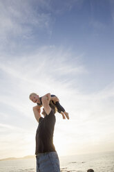 Mature man lifting up his toddler daughter on beach, Calvi, Corsica, France - CUF29837