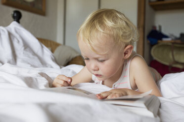 Weibliches Kleinkind liegt im Bett und liest ein Buch - CUF29839