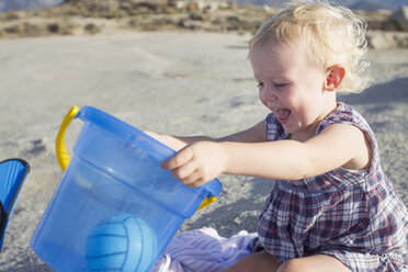 Happy female toddler playing on beach with toy bucket - CUF29842