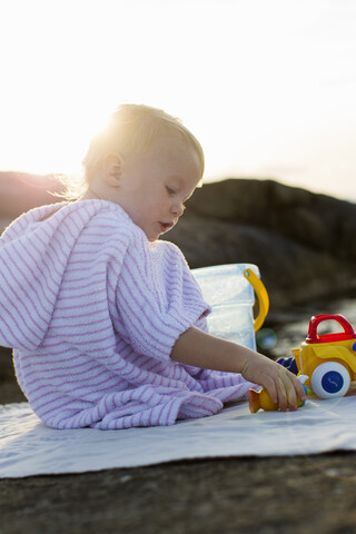 Weibliches Kleinkind sitzt am Strand und spielt mit einem Spielzeugeimer, lizenzfreies Stockfoto