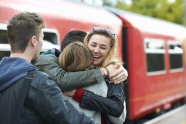 Gruppe von Freunden, die sich am Bahnhof umarmen, lächelnd - CUF29851