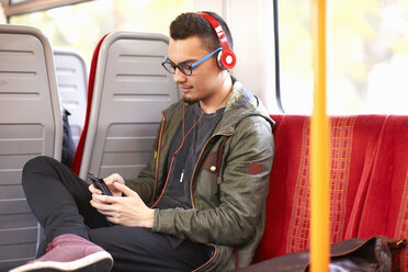 Young man sitting on train, using smartphone, wearing headphones - CUF29853