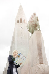Blick von unten auf ein jugendliches Mädchen, das neben einer Statue auf eine Karte schaut, Hallgrímskirkja, Reykjavik, Island - CUF29870