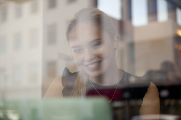 View through window of teenage girl using laptop computer looking down smiling, Reykjavik, Iceland - CUF29872